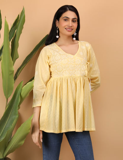 Woman wearing a yellow embroidered top with blue jeans against a beige background