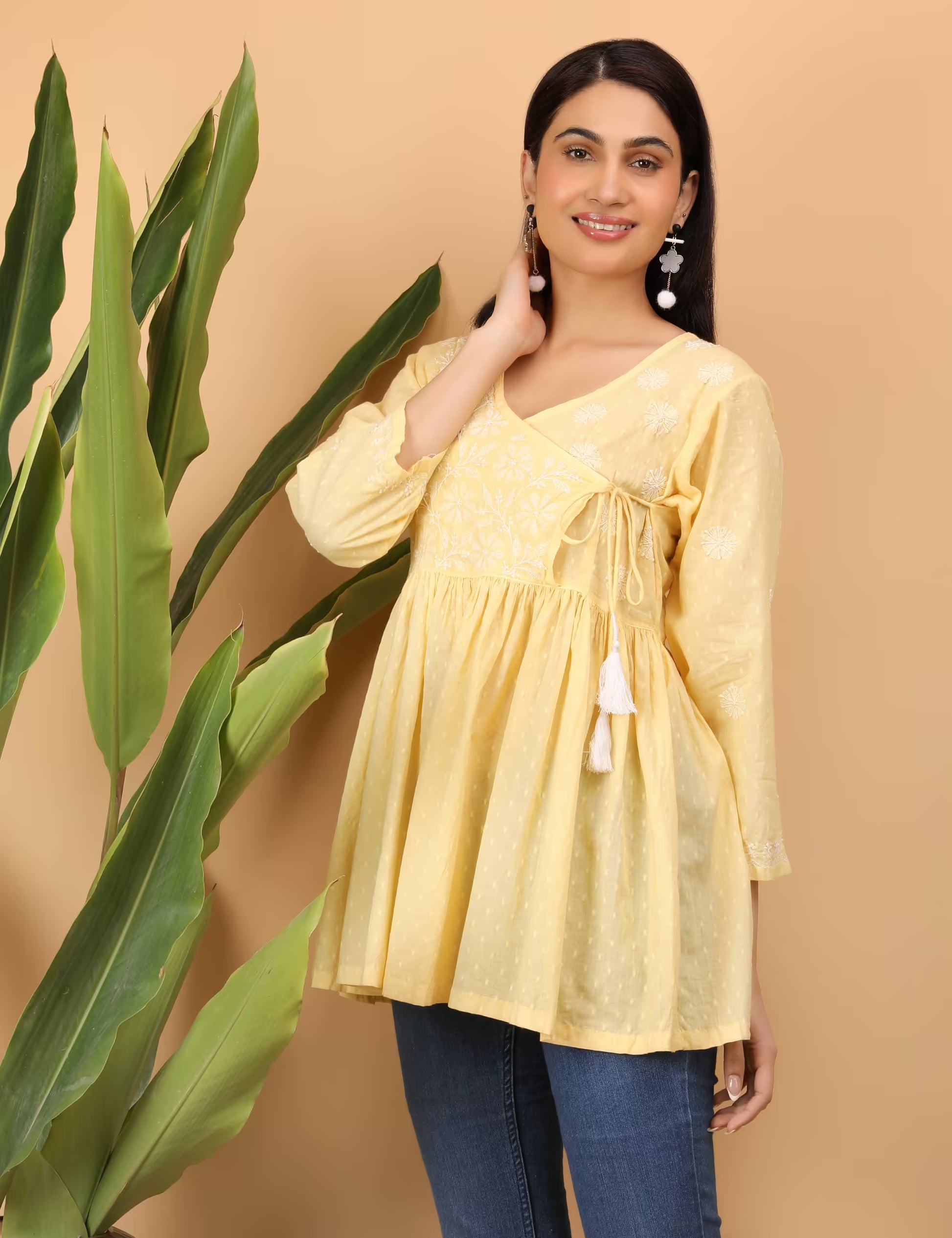 Woman wearing a yellow Top  with tassels against a beige background