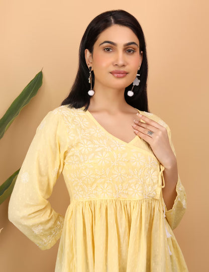 Woman wearing a yellow top with  Chikankari  patterns against a beige background