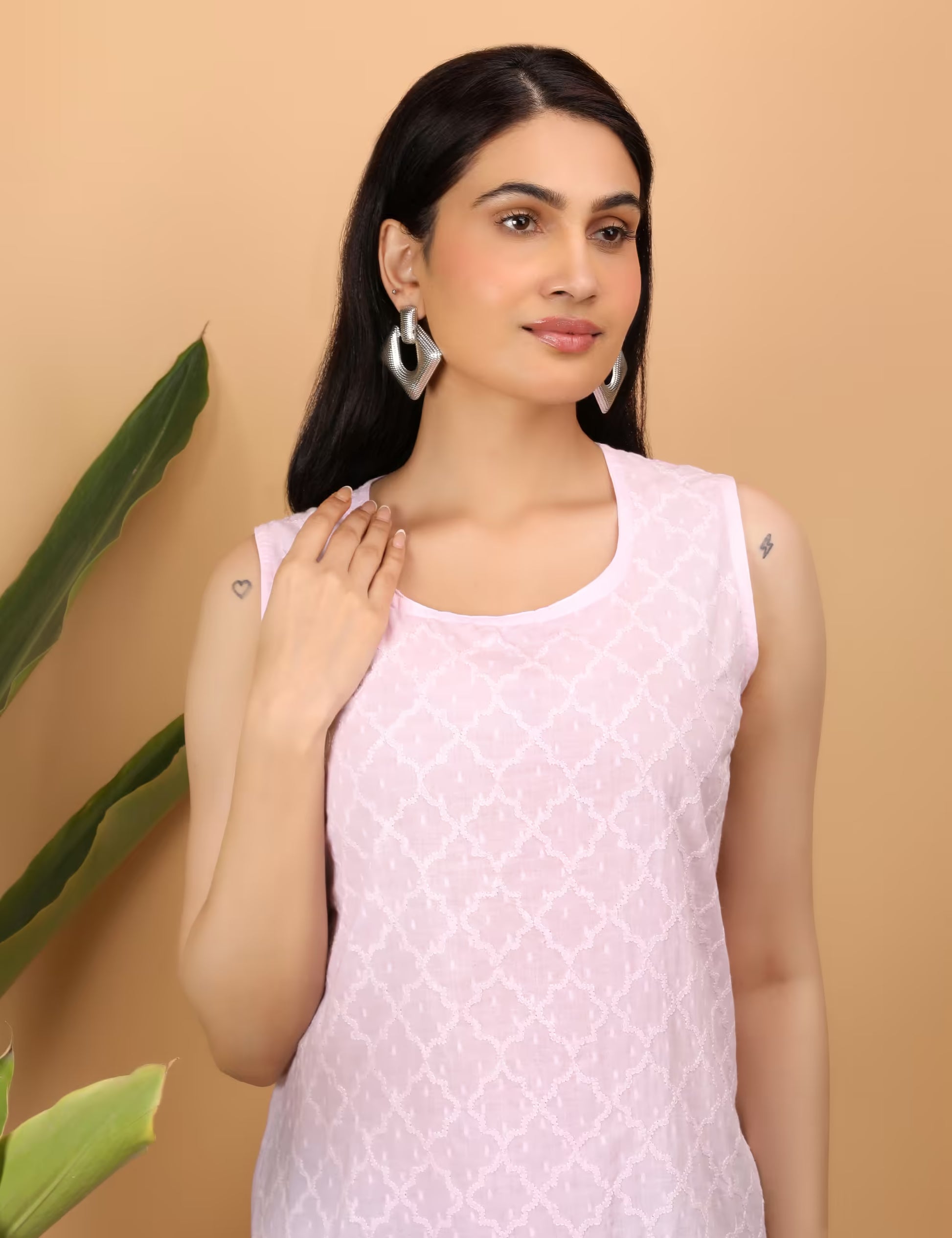 Woman wearing a light pink Chikankari sleeveless top with a subtle pattern against a beige background