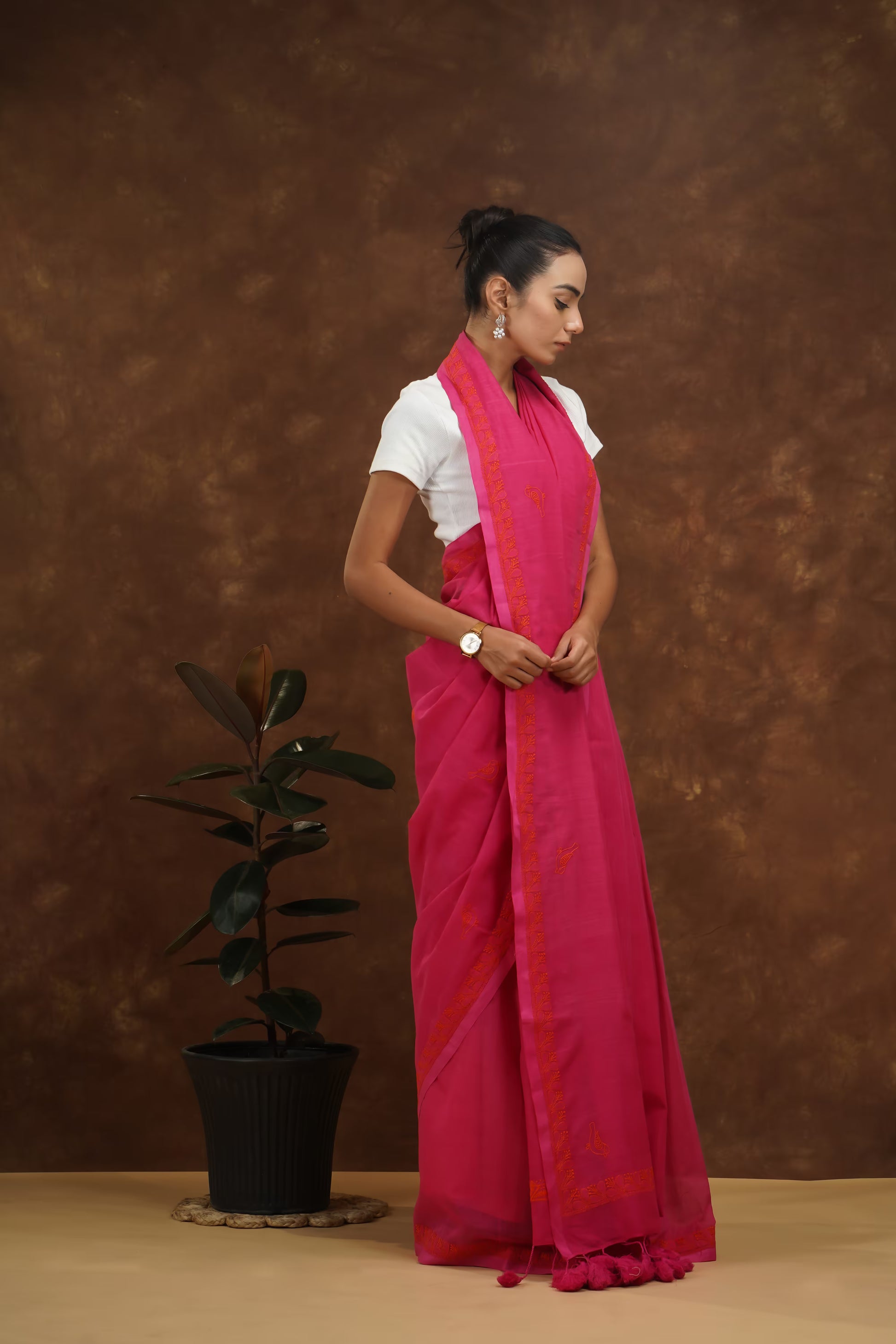 Woman wearing a megenta saree with a white blouse against a brown background