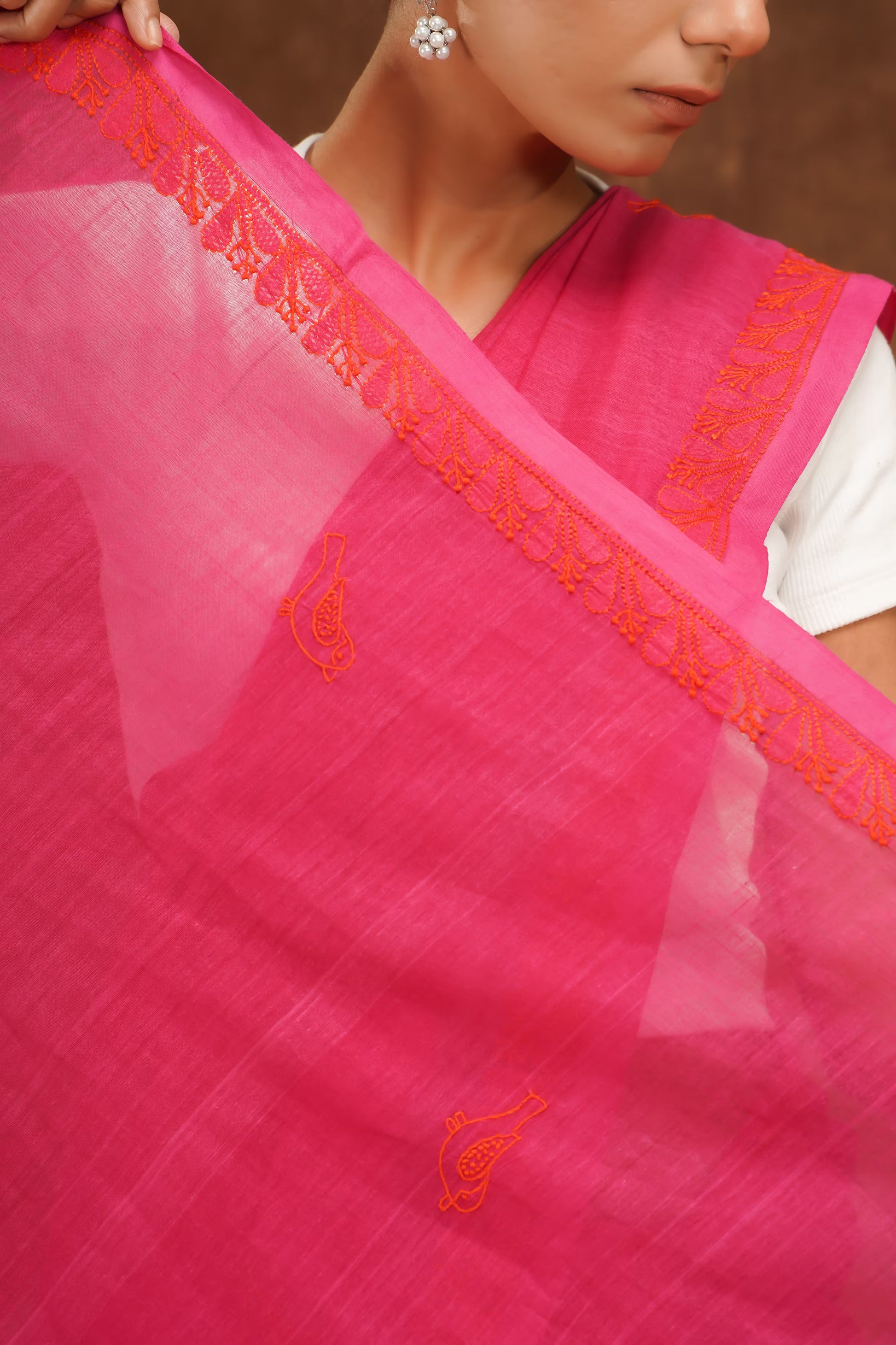 Close-up of a megenta saree with orange embroidery held by a person.