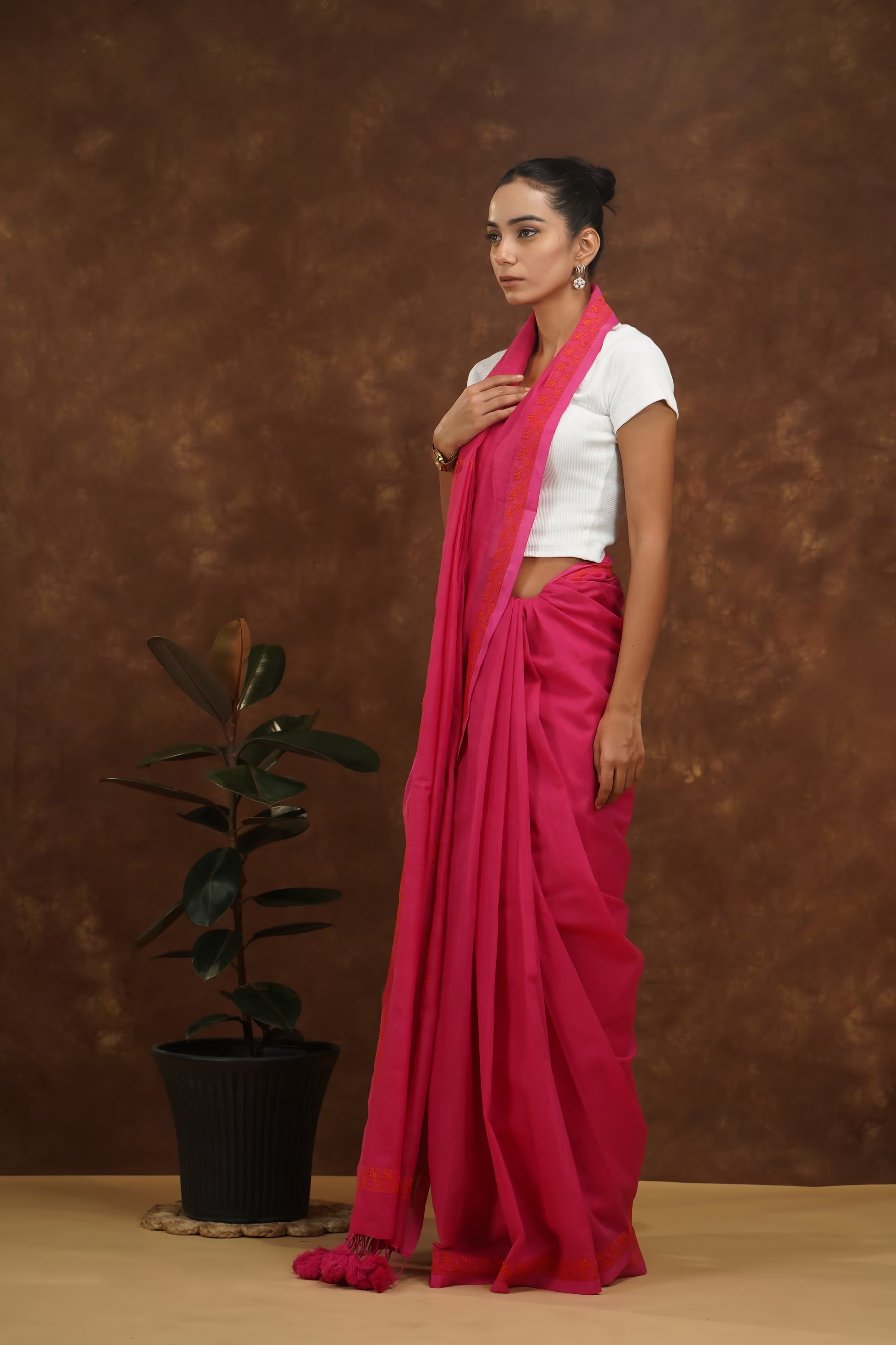 Woman wearing a megenta saree with a white blouse against a brown background