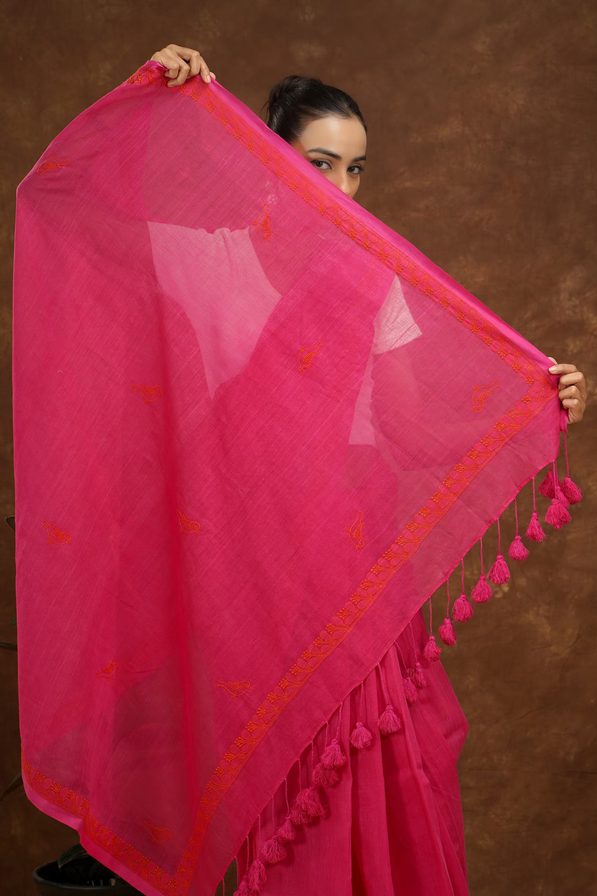 Woman holding a megenta saree with red patterns against a brown background