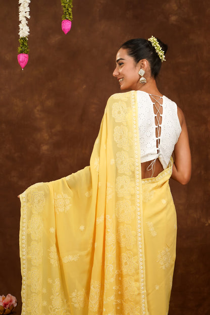 Woman in a yellow saree with a white blouse against a brown background