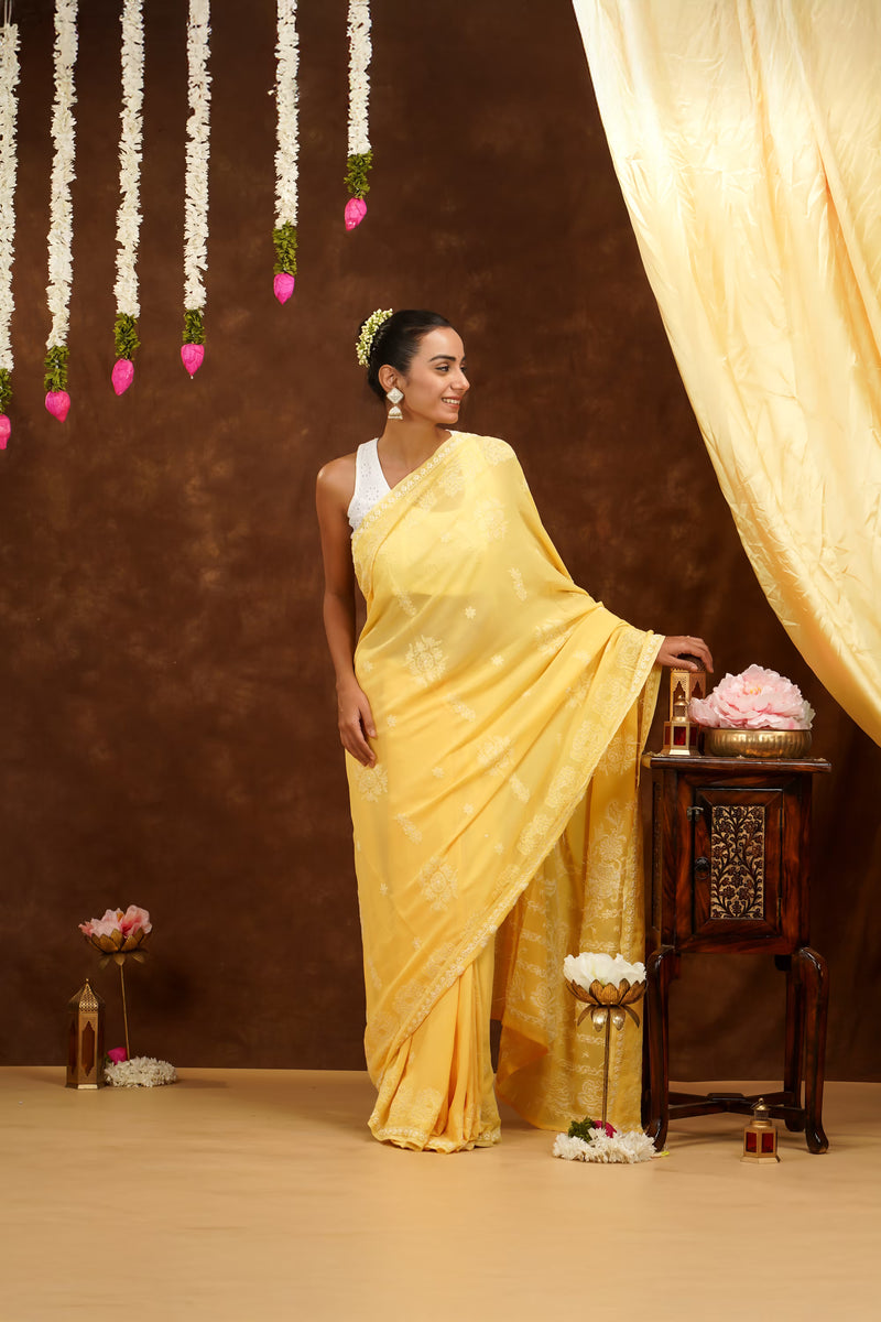 Woman in a yellow saree standing in a decorated room with flowers and curtains.