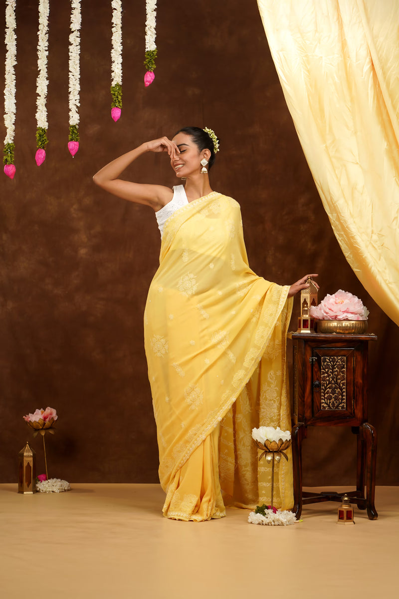 Woman in a yellow saree posing in a decorated room with flowers and a curtain.