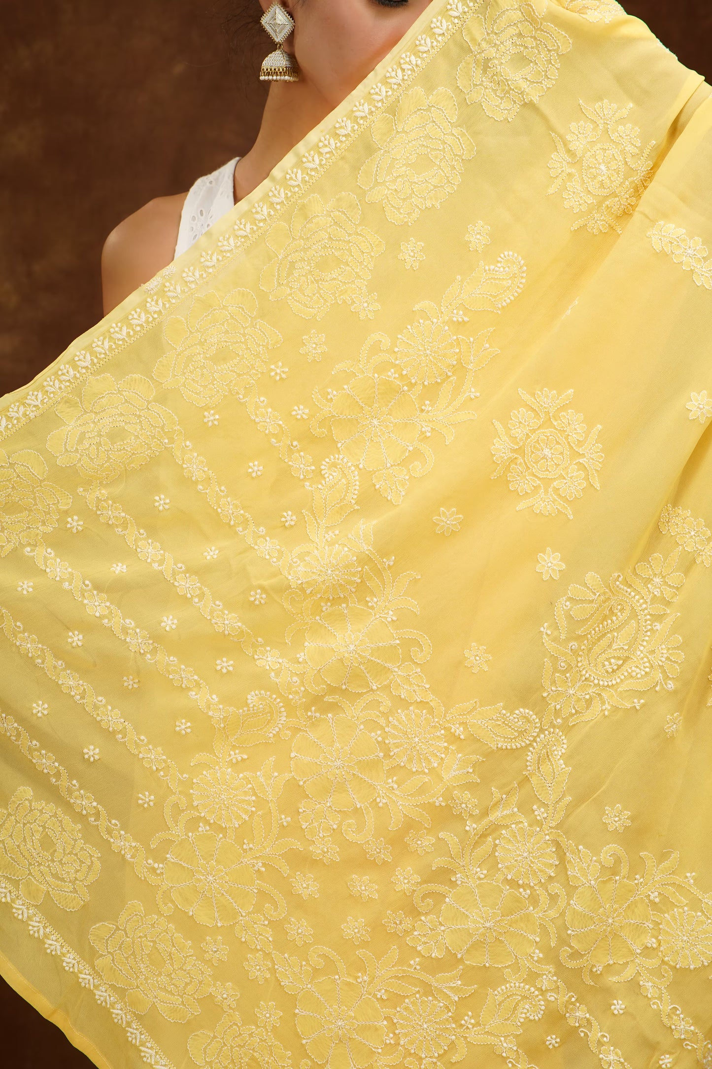 Yellow saree with intricate white patterns held by a person against a dark background