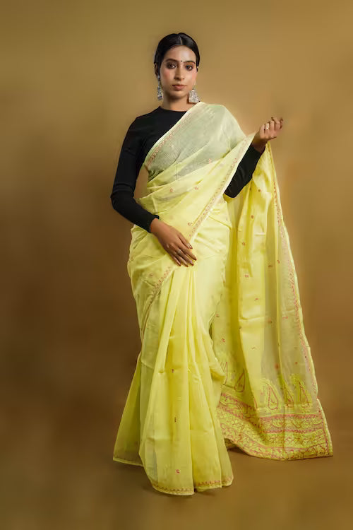 Woman wearing a light yellow saree with a black blouse against a beige background
