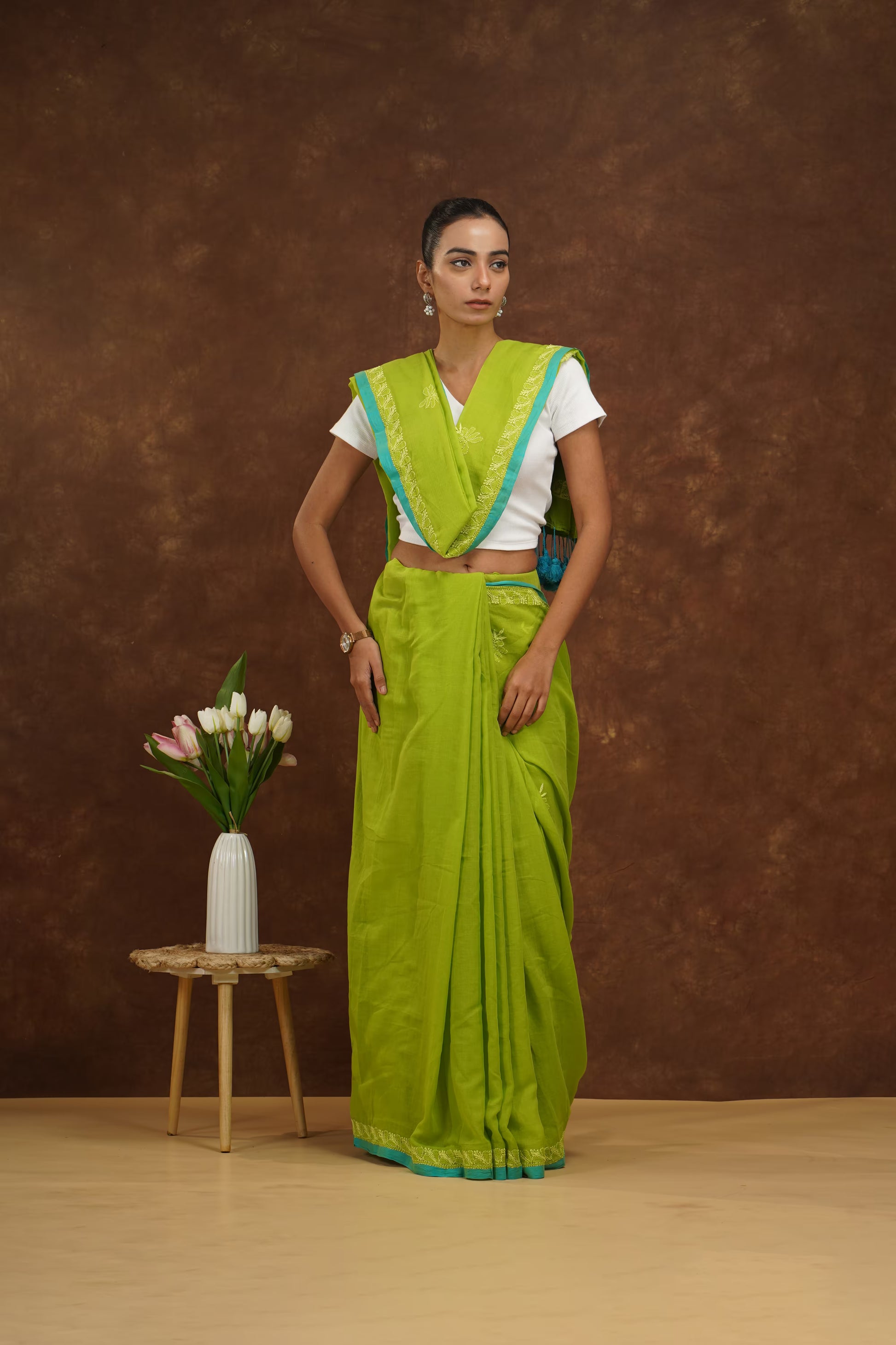 Woman in a parrot green saree with a white blouse against a brown background.