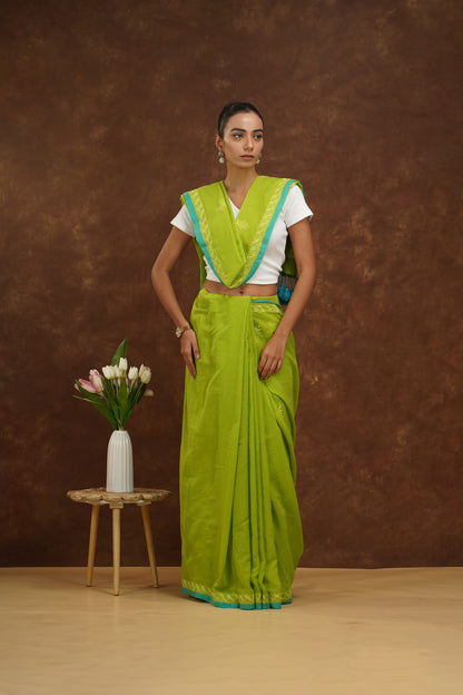Woman in a parrot green saree with a white blouse against a brown background.