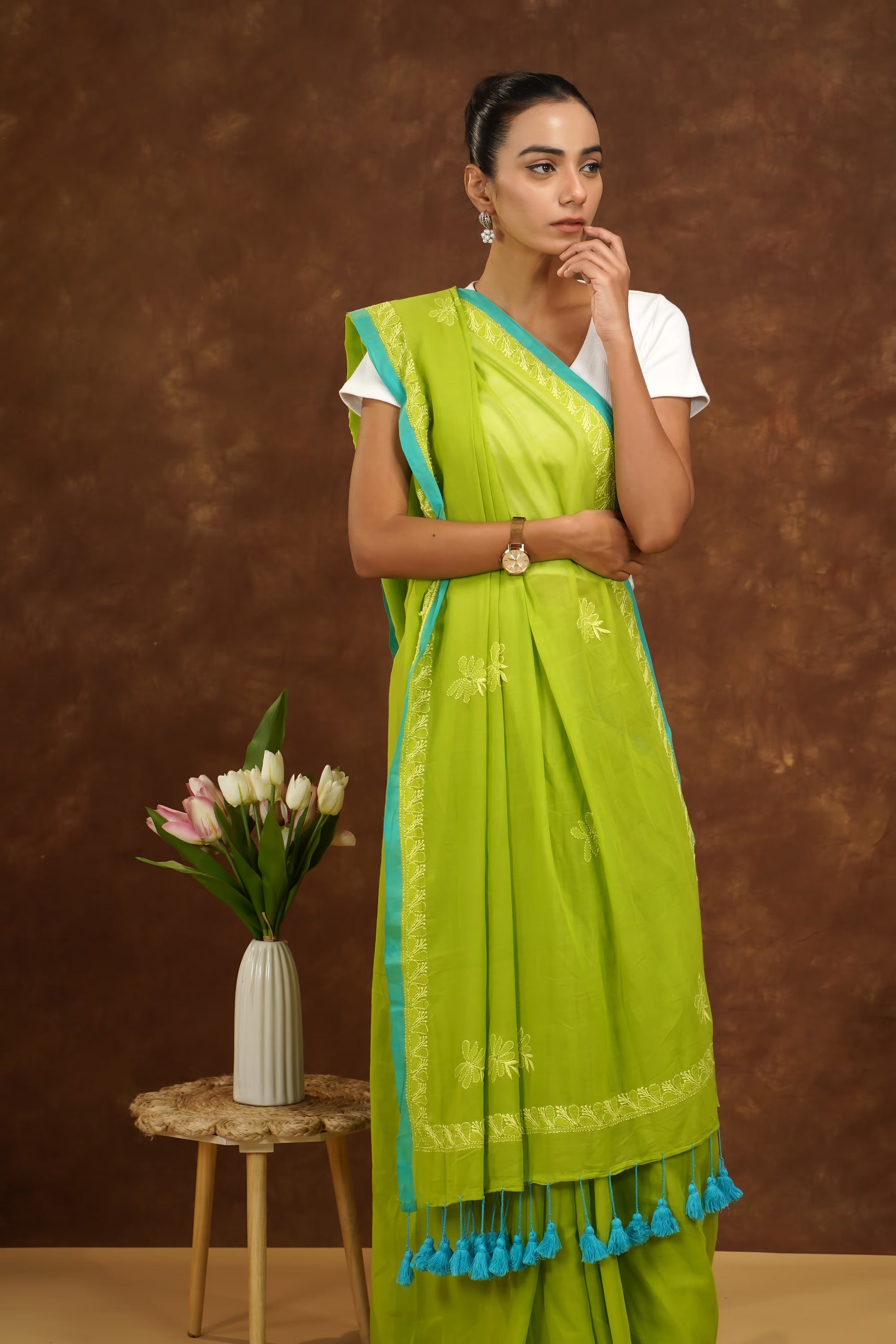 Woman in a parrot green traditional outfit with blue accents standing against a brown background