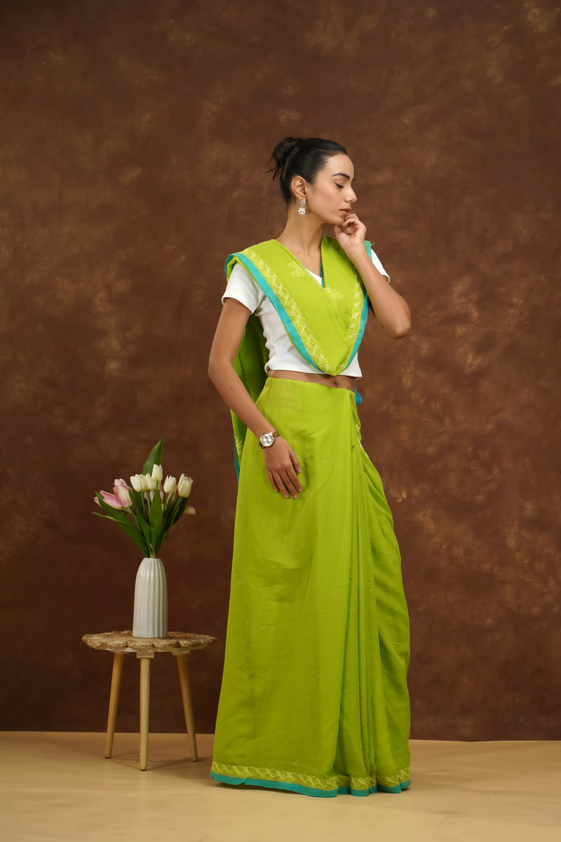 Woman in a parrot green saree with a white blouse against a brown background