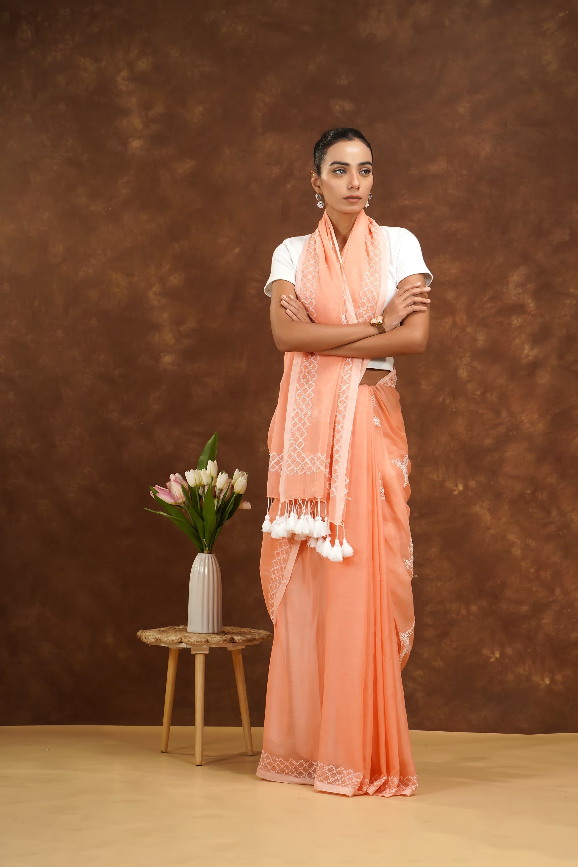 Woman wearing a peach saree with a white blouse against a brown background