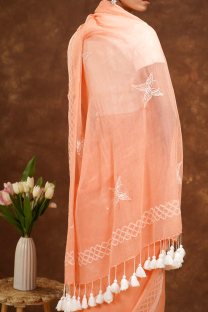 Peach-colored saree with white embroidery and tassels on a brown background.