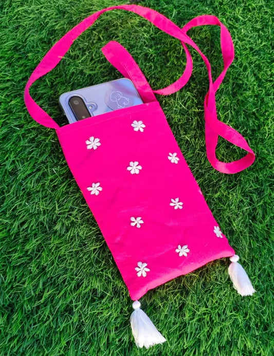 Pink pouch with white Chikankari patterns and tassels on a grass background