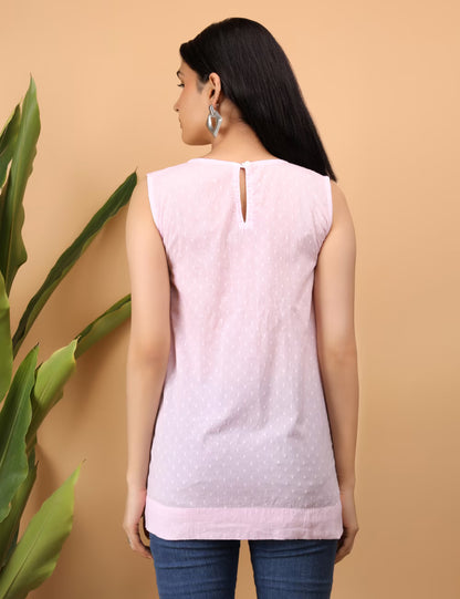 Woman wearing a light pink  chikankari sleeveless top with a cutout back design, standing against a beige background.