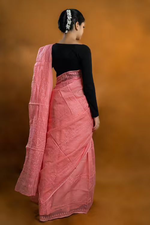Woman wearing a pink saree with a black blouse against an orange background