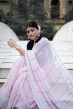 Woman in a light pink saree with a black blouse sitting on a bench.