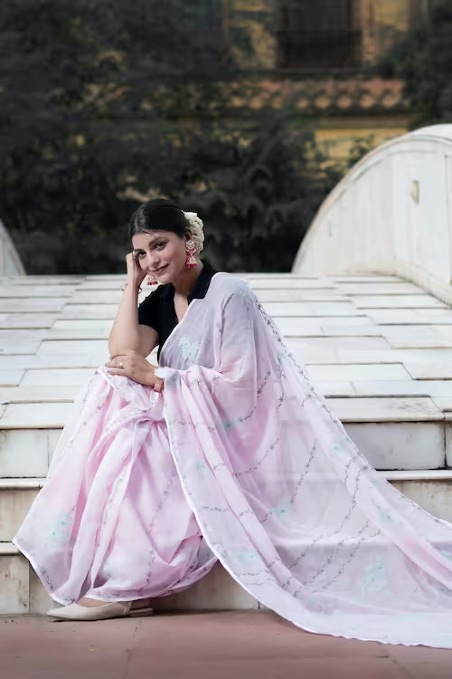 Woman in a pink saree sitting on steps with a blurred background