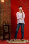 Woman in a pink top and blue jeans standing against a red wall with a wooden side table.