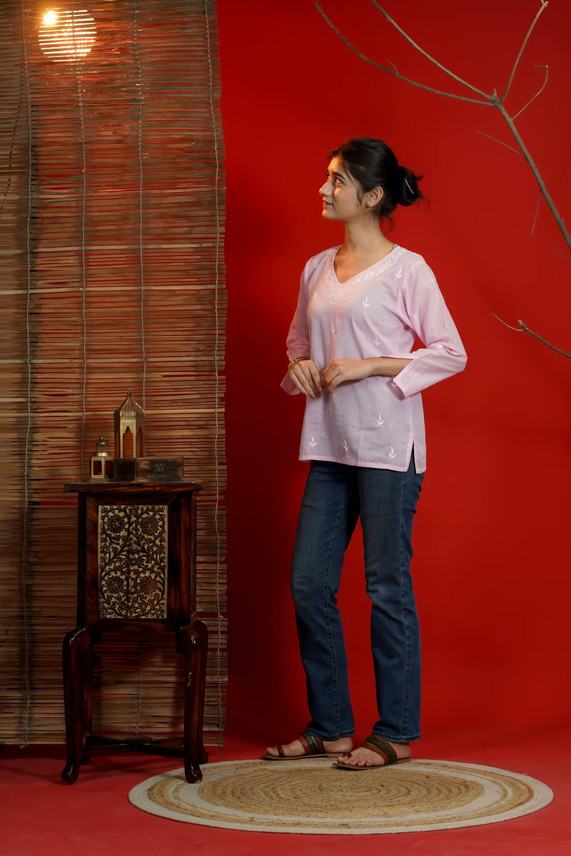 Woman in a pink top and blue jeans standing against a red wall with a wooden side table.
