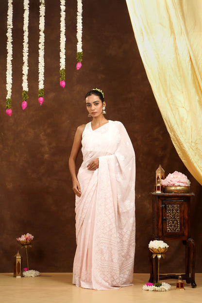 Woman in a white saree standing in a decorated room with flowers and a curtain.
