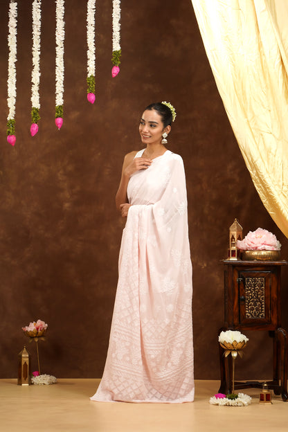 Woman in a white saree standing in a decorated room with flowers and a curtain.