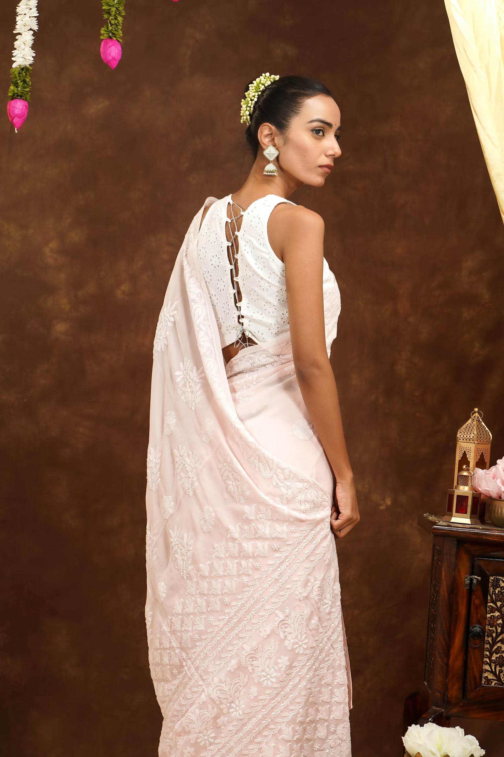 Woman in a white saree with intricate designs against a brown background