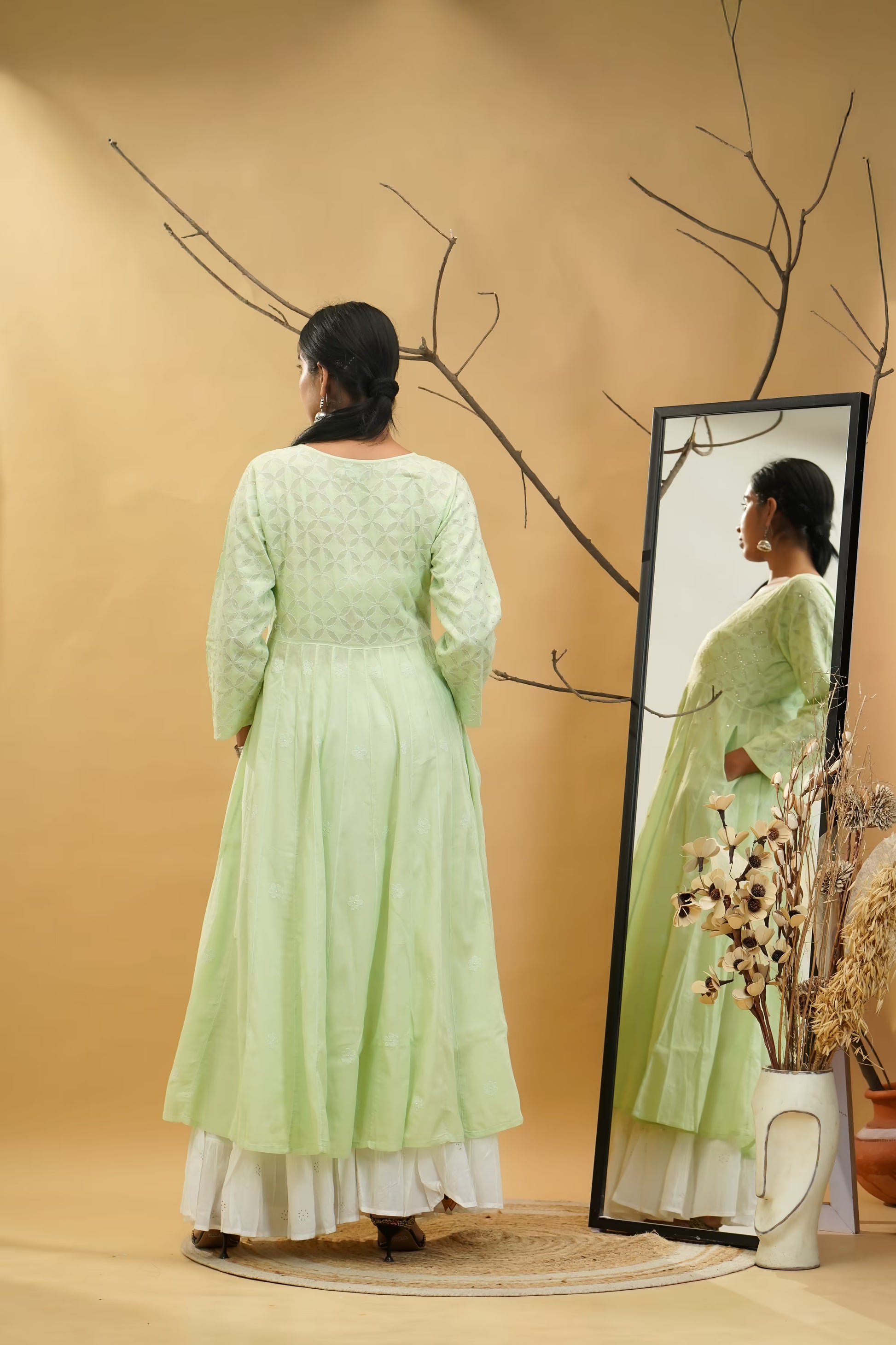 Woman in a light green dress standing in front of a mirror on a beige background