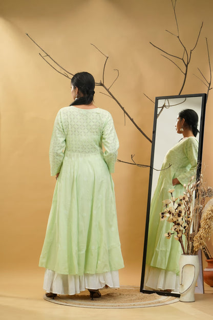 Woman in a light green dress standing in front of a mirror on a beige background