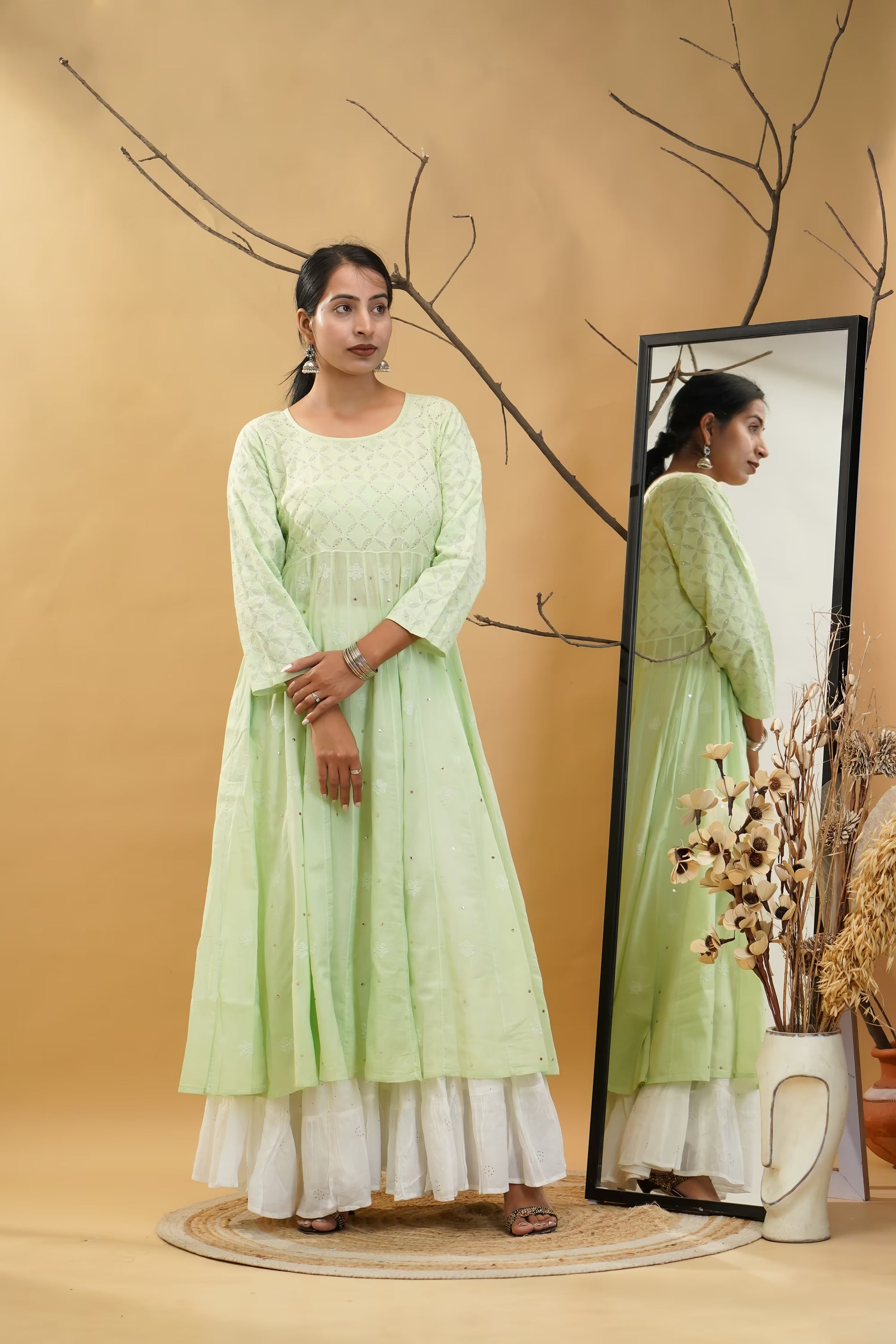 Woman in a pista green dress standing next to a mirror on a beige background