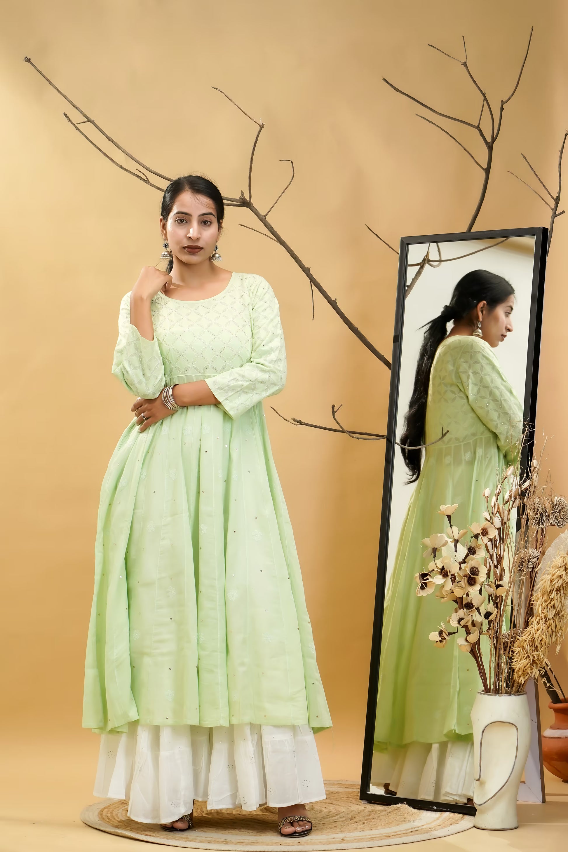 Woman in a pista green dress standing next to a mirror with a beige background