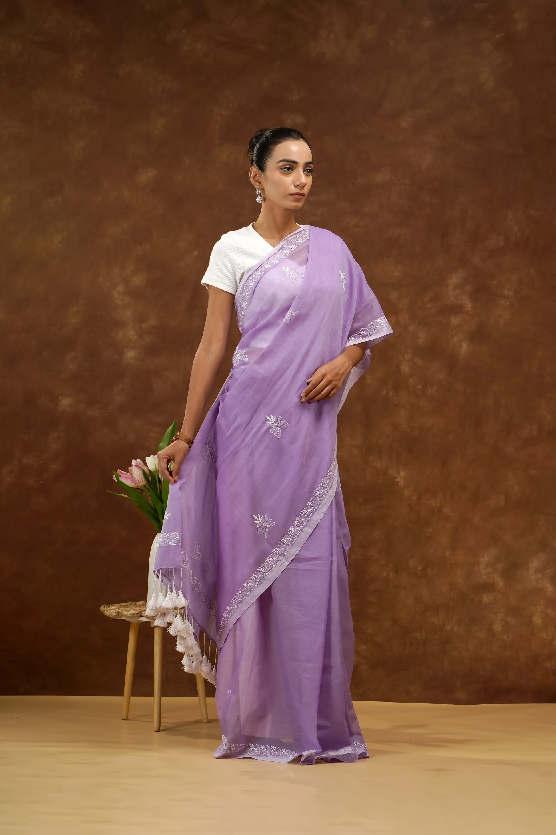 Woman wearing a purple saree with a white blouse against a brown background