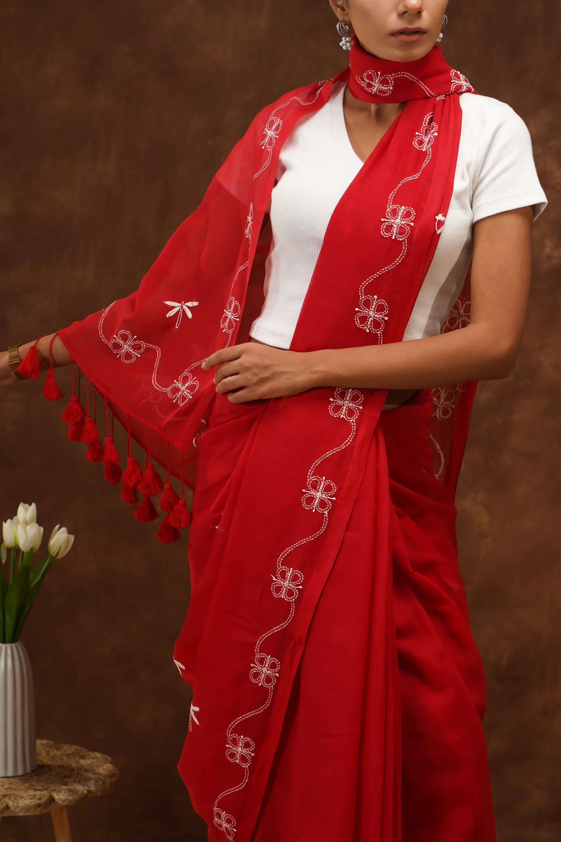 Woman wearing a red saree with white patterns and tassels against a brown background