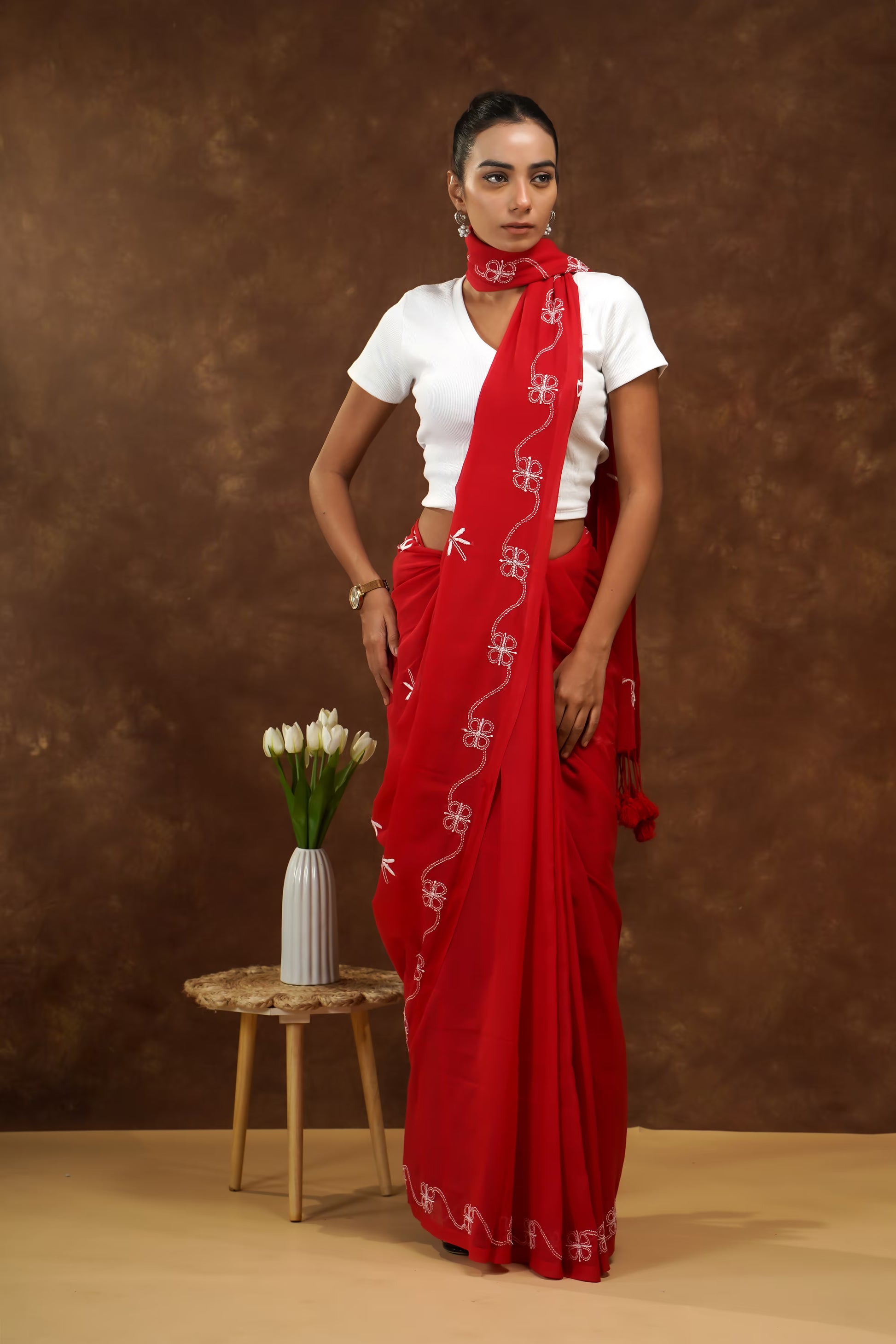 Woman wearing a red saree with a white blouse against a brown background
