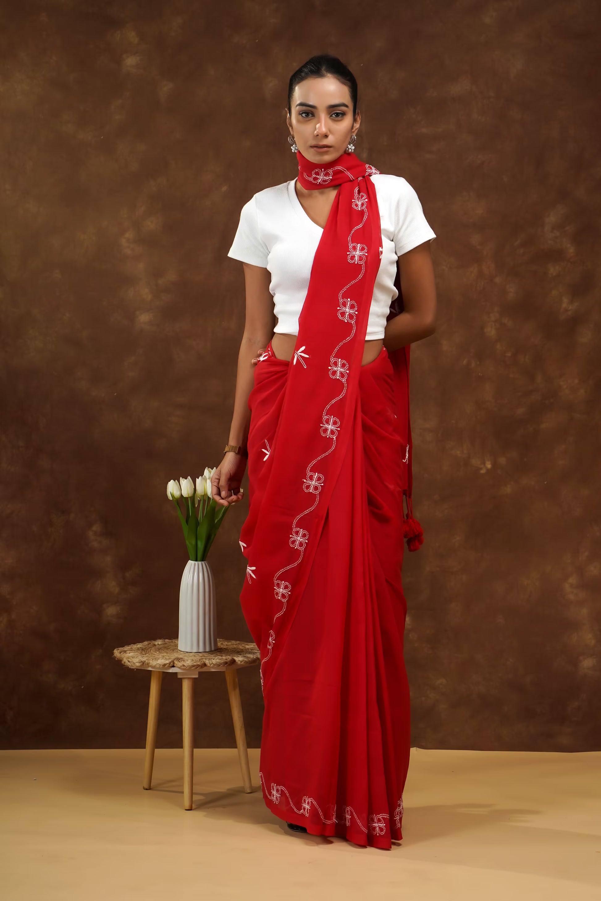 Woman wearing a red saree with white patterns against a brown background