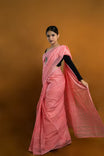 Woman wearing a pink saree with a black blouse against an orange background