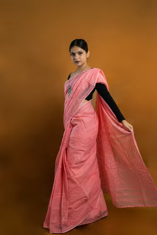 Woman wearing a pink saree with a black blouse against an orange background