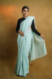 Woman wearing a light blue saree with a black blouse against a warm brown background