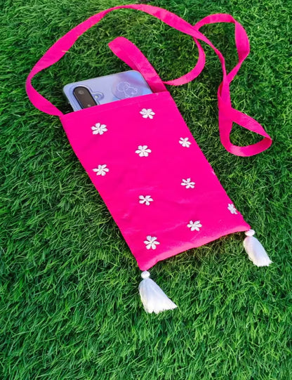 Pink crossbody bag with white floral patterns and tassels on a grass background
