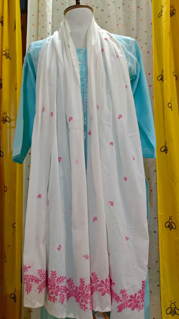 White scarf with pink Chikankari  patterns draped over a turquoise garment on a mannequin against a yellow curtain background.