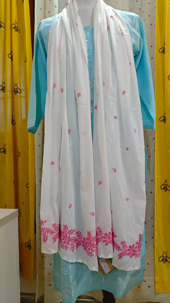 White scarf with pink Chikankari patterns draped over a blue garment against a patterned wall.