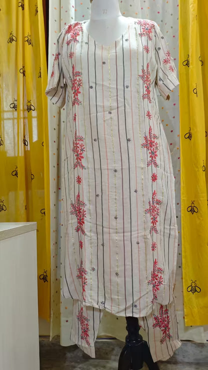 White dress with red Chikankari  patterns on a mannequin against yellow curtains.