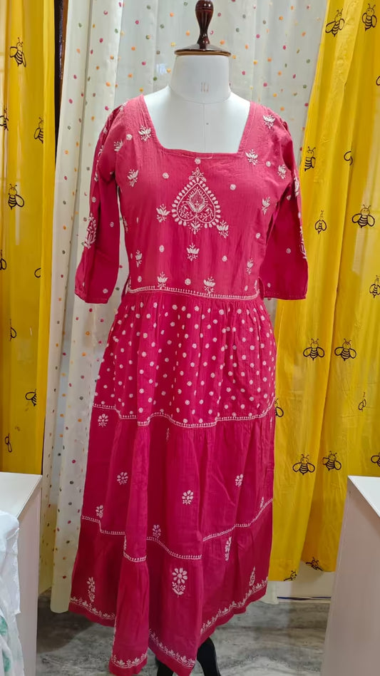 Pink dress with white Chikankari patterns on a mannequin against yellow and white curtains.