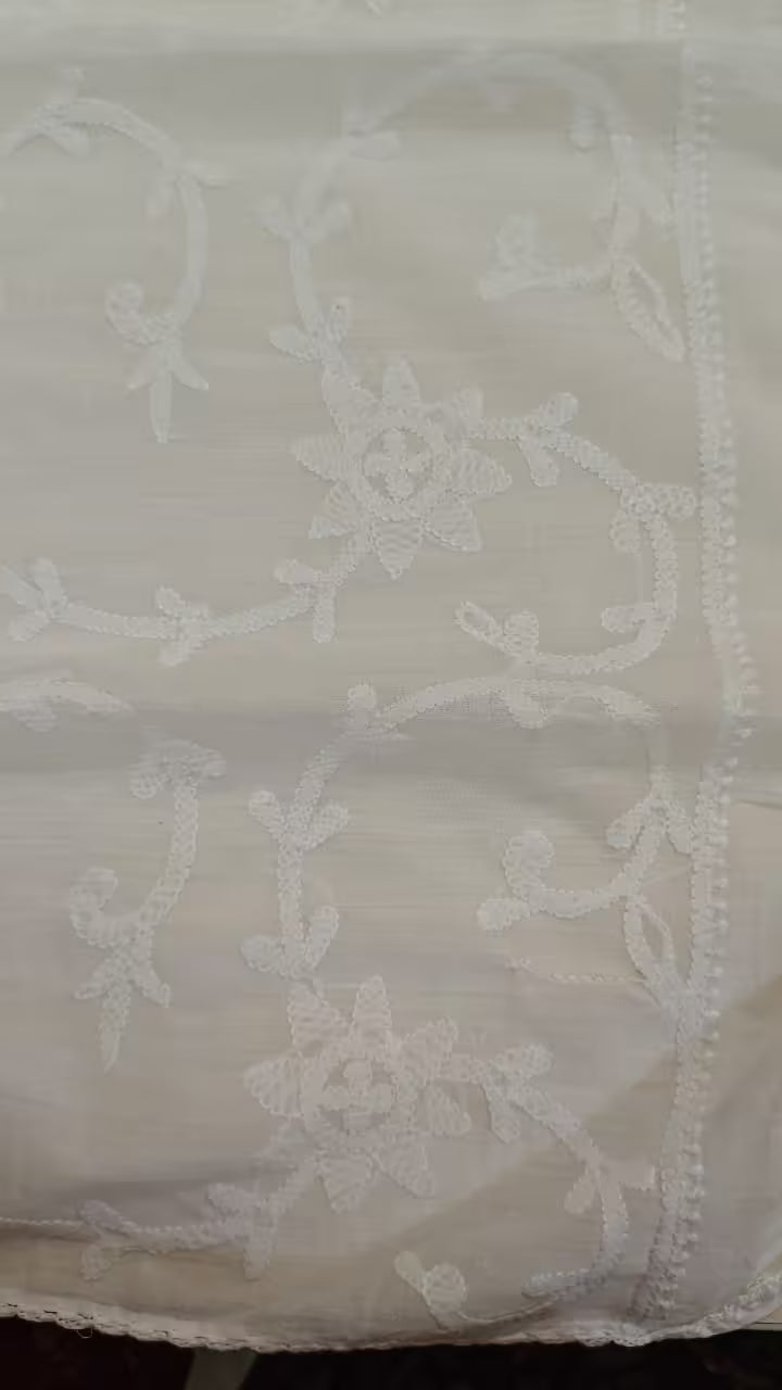 White lace fabric with intricate Chikankari patterns on a plain background