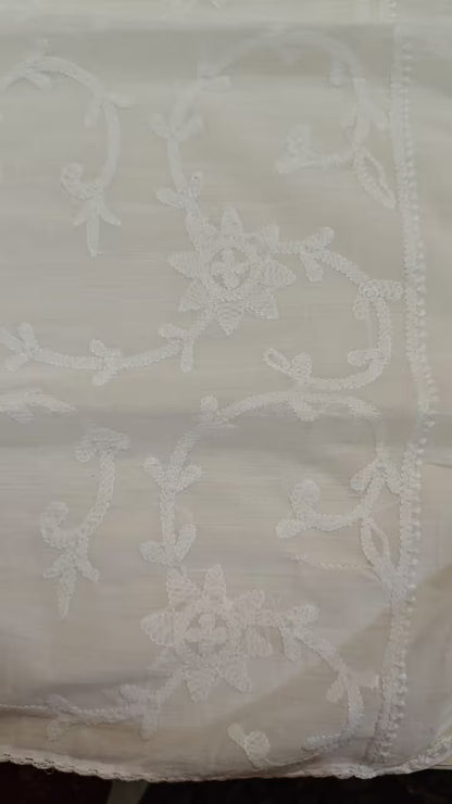 White lace fabric with intricate Chikankari patterns on a plain background