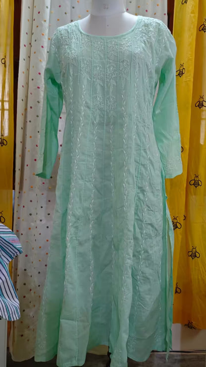 Mint green embroidered Chikankari dress on a mannequin against a yellow curtain background