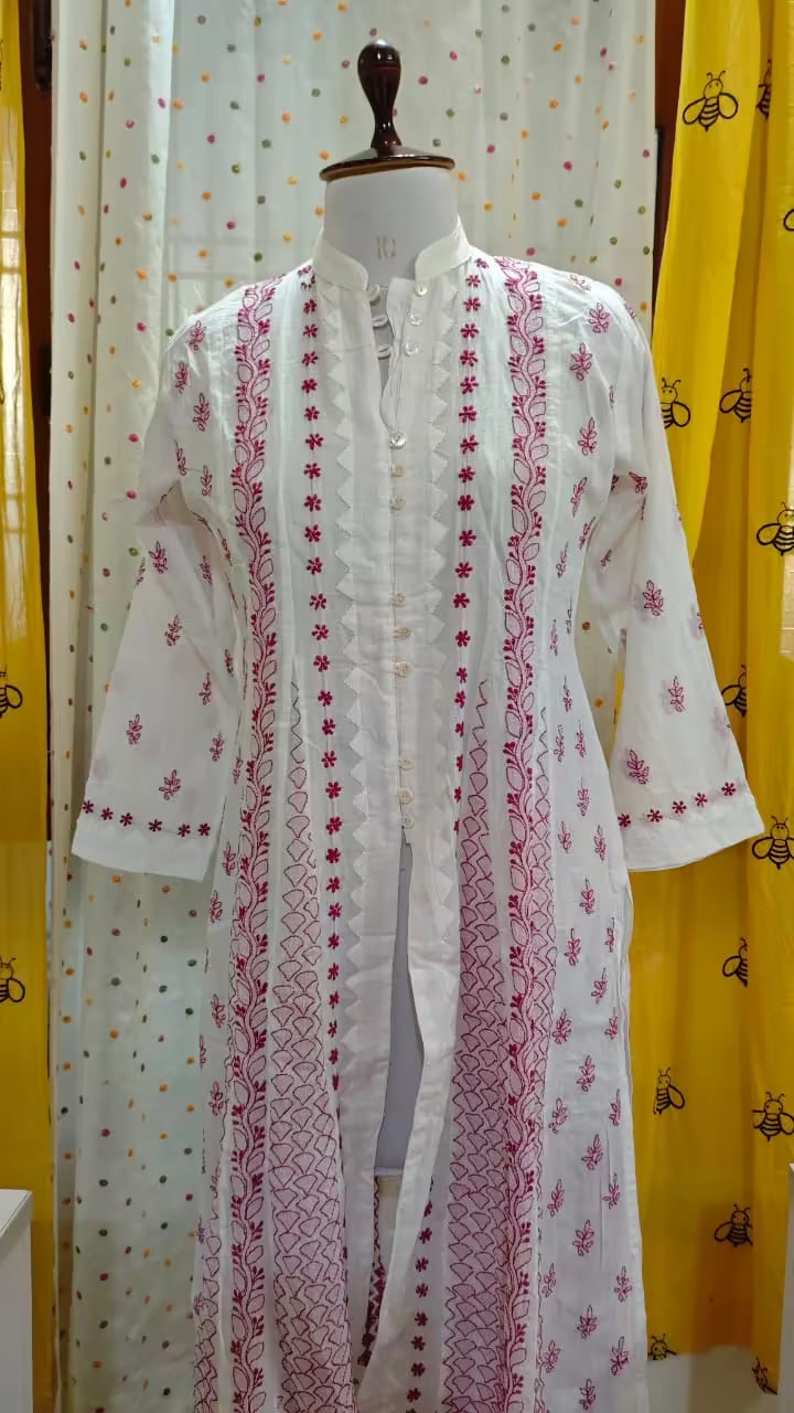White embroidered kurta with pink  Chikankari patterns on a mannequin against a yellow curtain background