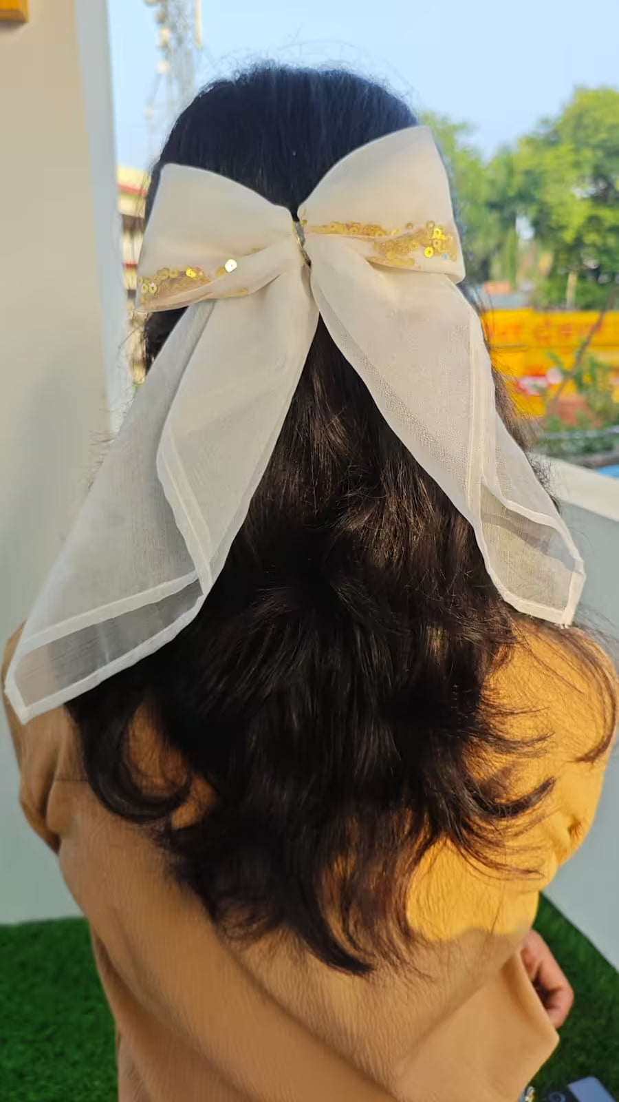 Person with a large white bow in their hair outdoors
